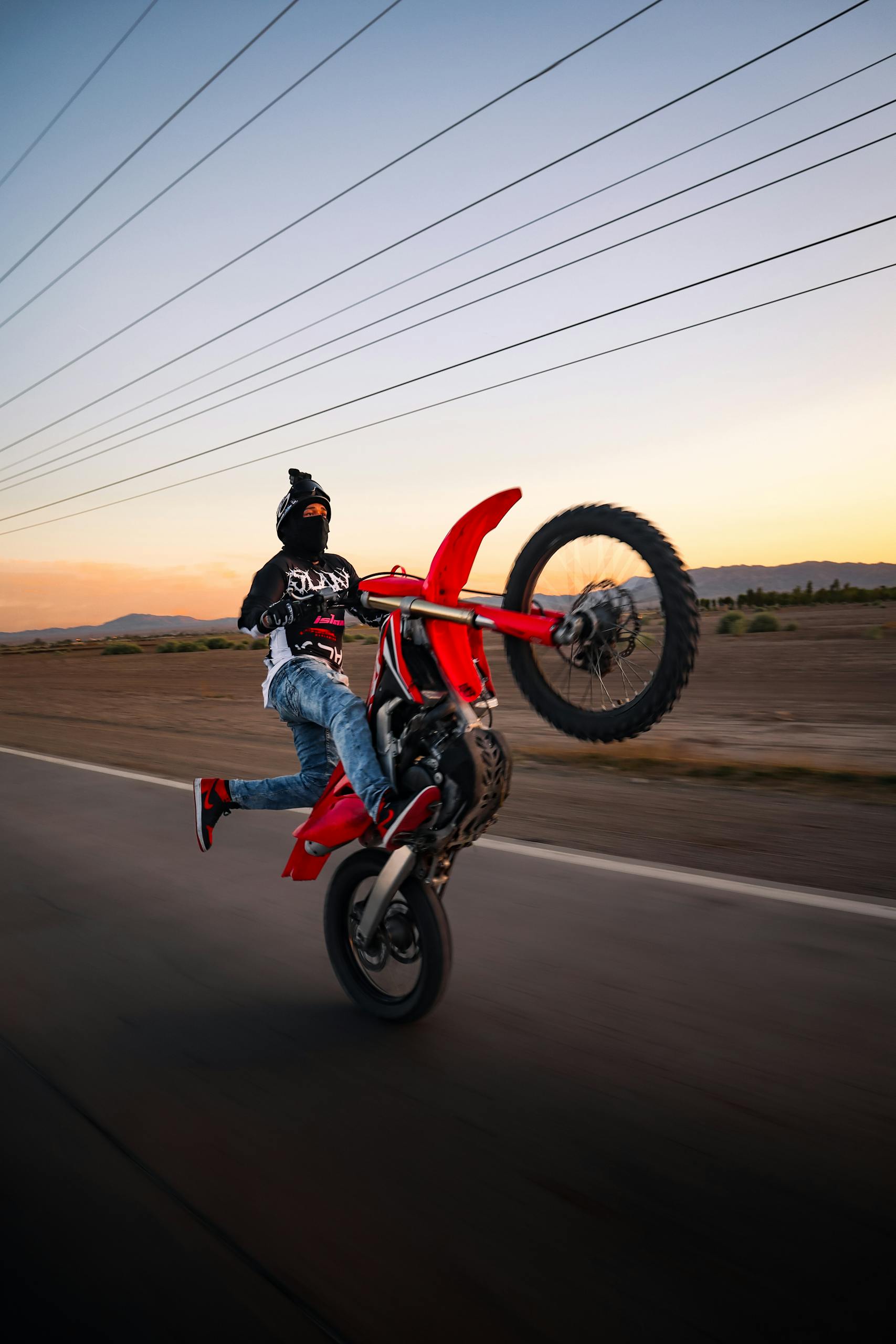 Thrilling stunt of a motorcyclist executing a wheelie on a deserted road during a stunning sunset.