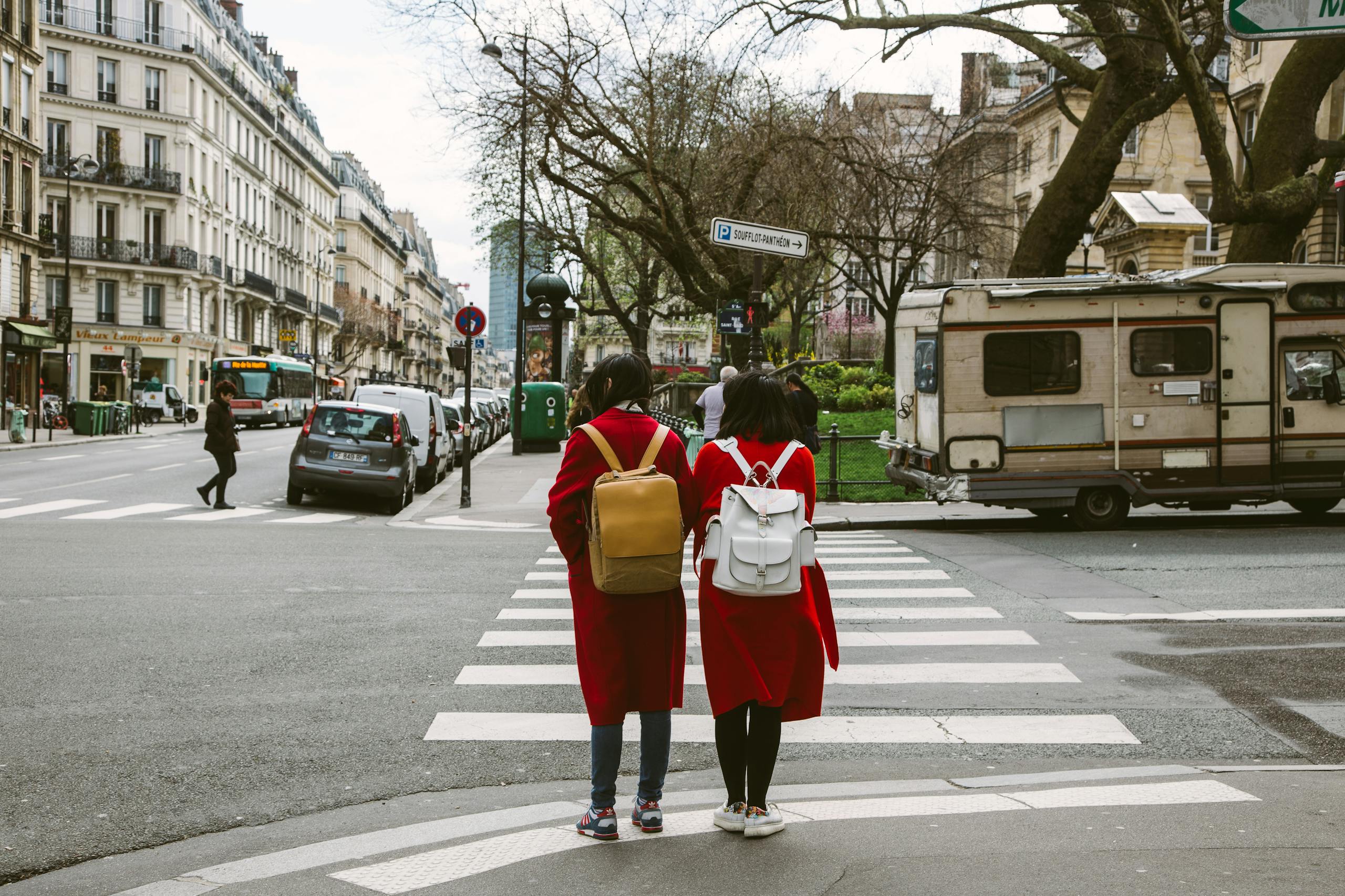 Two women in red coats crossing a Paris street at a zebra crossing.